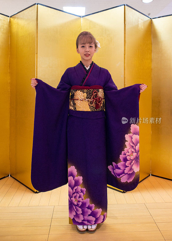 身着Furisode和服的日本妇女站在“Seijin Shiki”成人礼的金色“Byo-bu”折叠屏风前的肖像